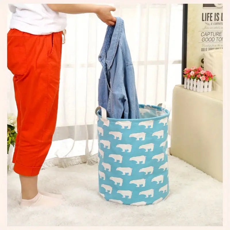 A person placing a shirt into the blue Large Capacity Cotton Linen Laundry Basket featuring white polar bears by PureAura.