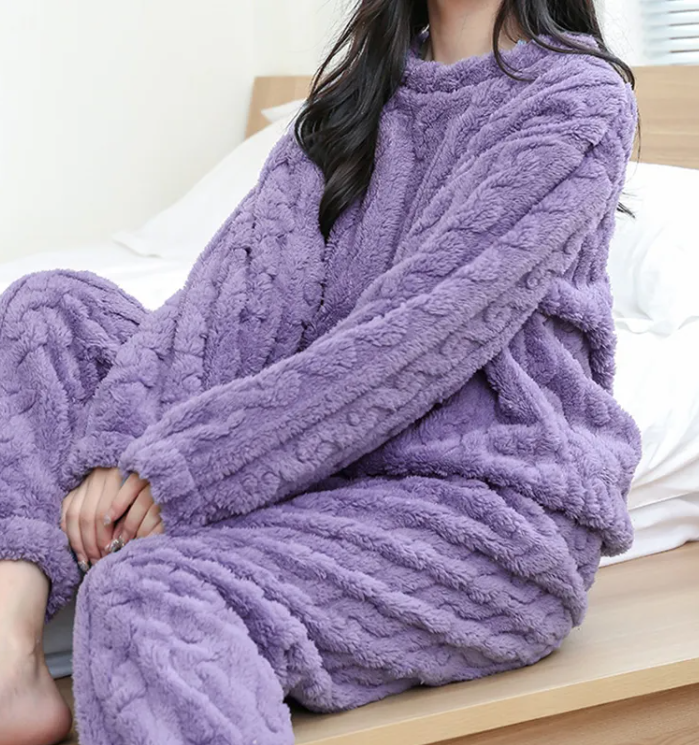 Cozy model seated on a bed wearing a plush purple Winter Coral Velvet Pajama Set by PureAura.