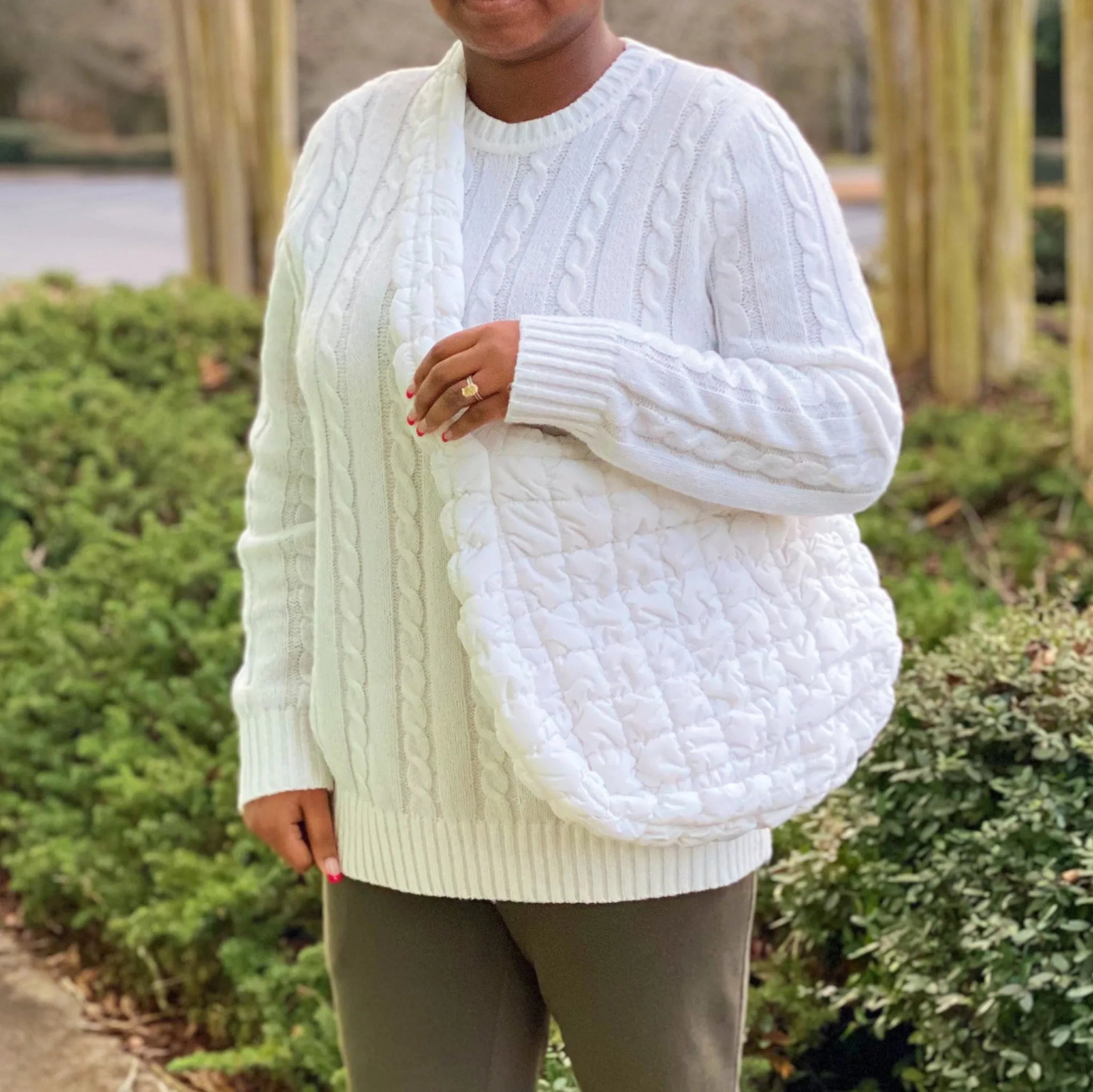 A woman wears a white Carry All Quilted Cross Body Bag, showcasing its soft texture against her cozy outfit by My Store.